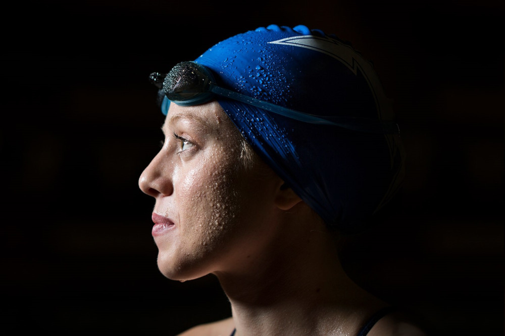 A woman in a blue swimming cap, dripping with water, staring off to the side, focused.